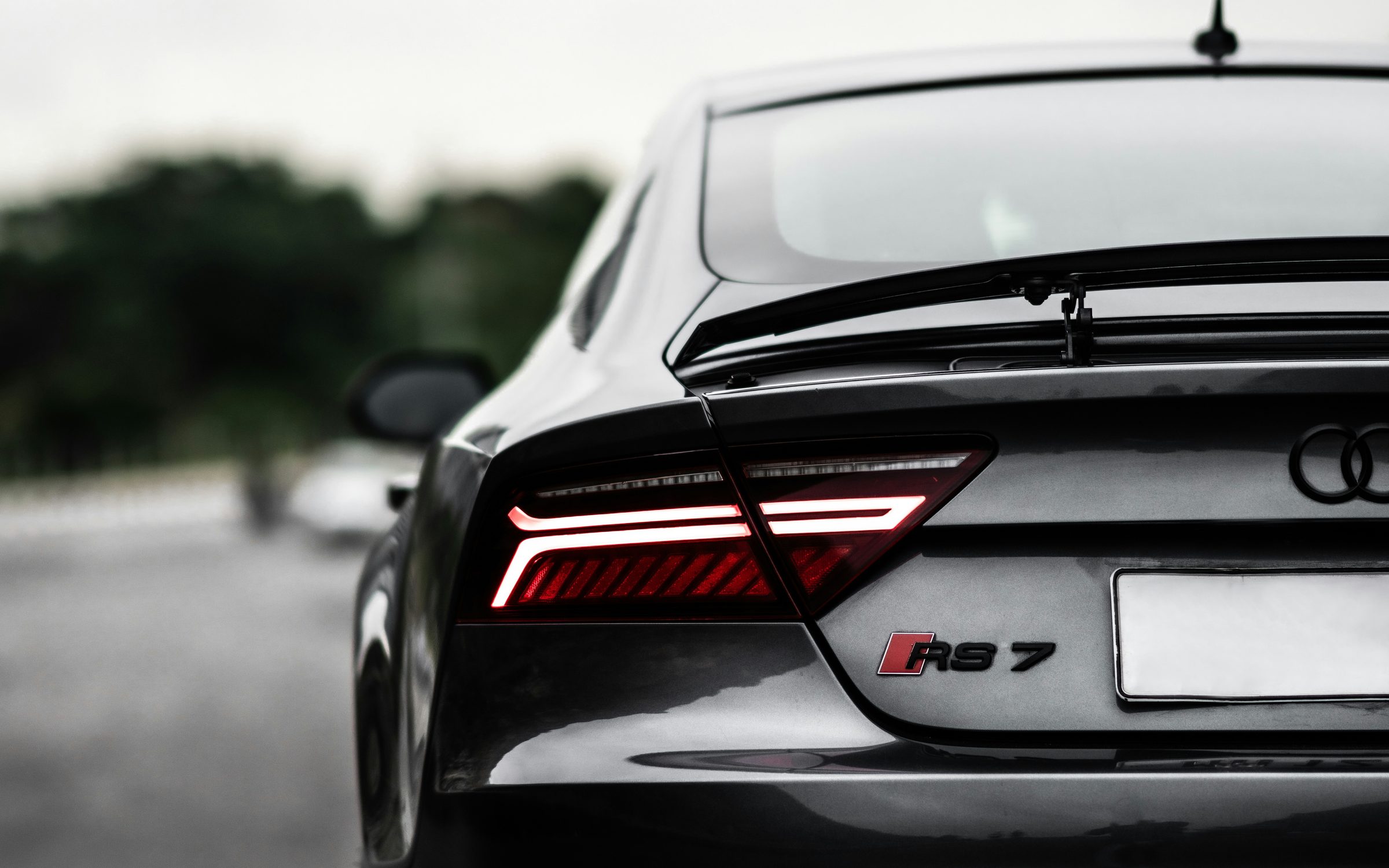 The rear of a black Audi RS 7 Sportback on a wet road, tail lights lit.